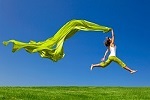 Beautiful young woman jumping on  a green meadow with a colored tissue